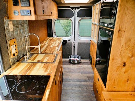 Gusto 3 rental van interior with murphy bed stowed up against wall provides lots of kitchen counter/prep space and walk through to back door