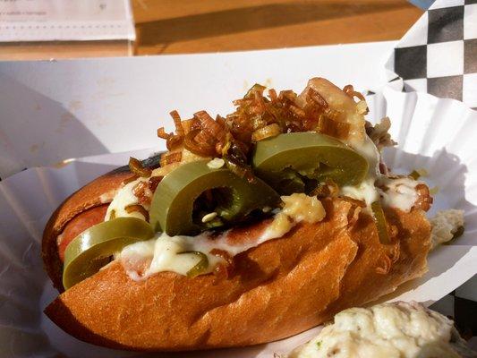 A partially eaten Bourgeois Dog with added jalapenos. Potato salad in extreme foreground.