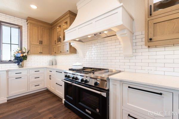 Black Kitchen Aide gas stove with double ovens, painted white wood hood and glass cabinet doors