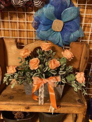 This is a bouquet of peach color roses, along with greenery, and a peach and lace ribbon. In the background us another wreath.