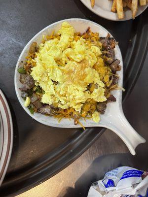 Steak skillet with hash browns, green paper and onion, and cheese  topped with eggs