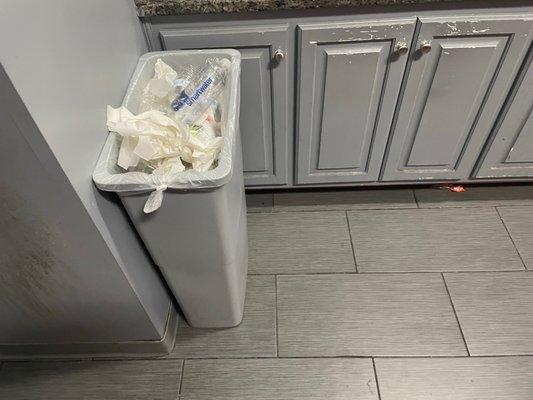 Overflowing trash can in men's restroom