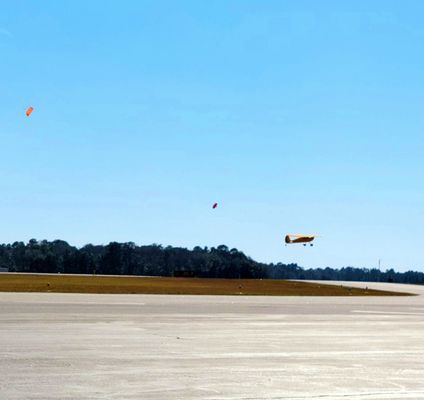 Plane taking off while 2 sky divers land in the distance