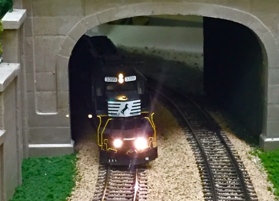 An HO-scale Norfolk Southern engine  emerging from a tunnel on the layout.