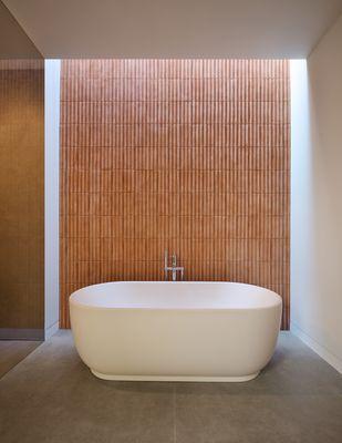 Daylight pours down a terracotta wall behind this freestanding tub.