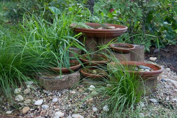 A simple bird bath built from catalpa logs and surrounded by native sedges, shrubs, and flowering plants.