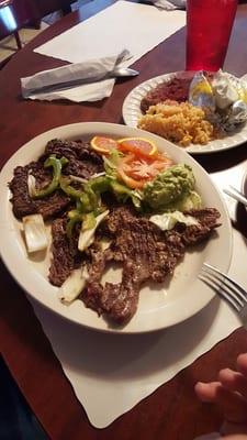 Fajita plate with rice, beans, baked potato, and homemade flour tortillas. A side of salad and guacamole.