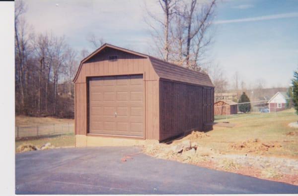 Dark brown shed with timberbland shingles.  Has garage door and concrete slab that are optional.