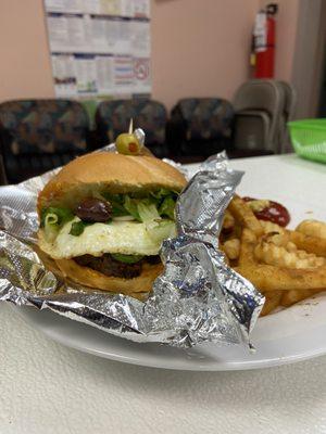 Homemade burger with egg, olives, salad and fries on the side.