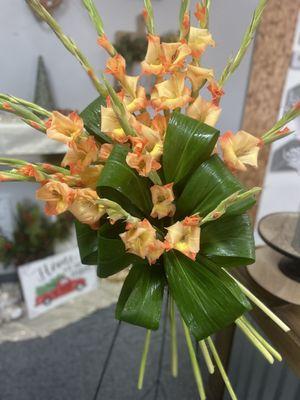 A bright and unique standing spray of orange gladiolas and sculpted tropical foliage.  Sophisticated yet simple.