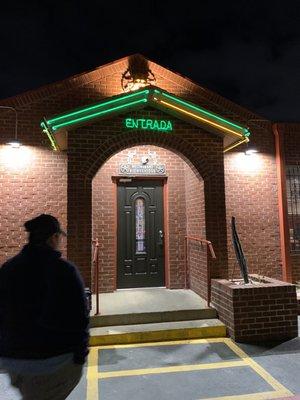 The green entrance sign on the side of the building opposite the driveway