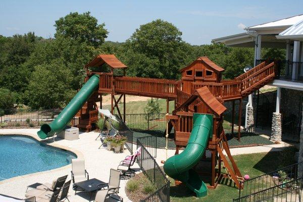 Custom redwood playset bridged to forts and to 2nd story of home with slide accessing swimming pool.