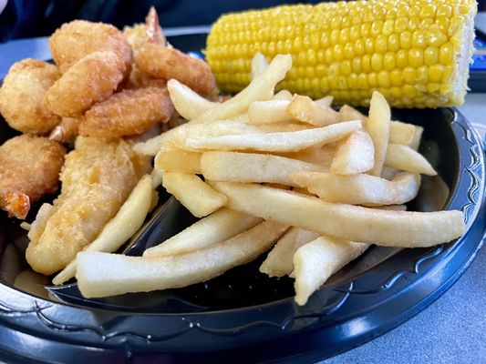 Fish and shrimp senior meal with corn on the cob and French fries.