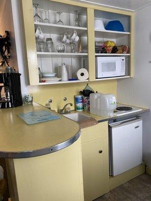 Kitchenette with microwave, mini fridge, sink, coffee maker, range top, and dishes.