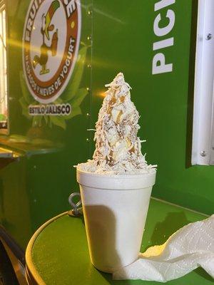 Nieve de yogurt chica con coco rayado, durazno en almíbar, almendras y cajeta.