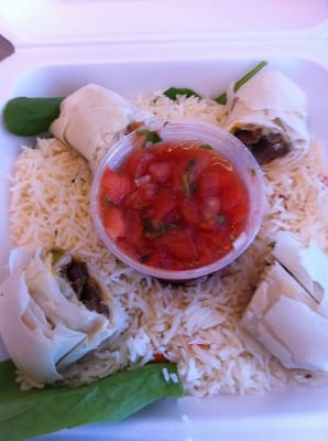 Steak fajita egg rolls on rice with spinach leaves