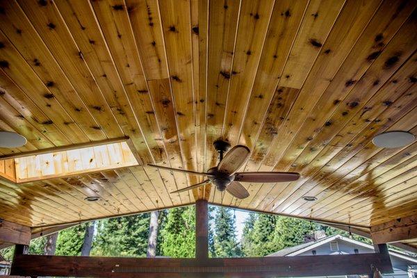 The patio's vaulted ceiling features tongue and groove cedar, a skylight, a wooden fan, can lighting, and scissor trusses.