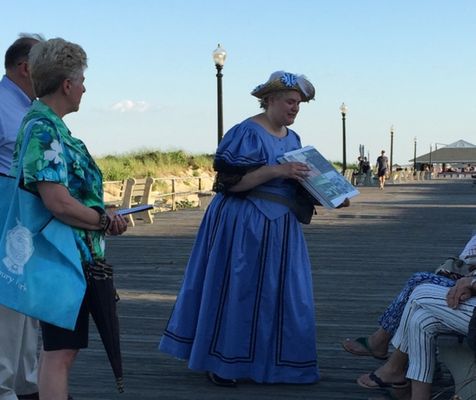 A guide in Victorian costume shares photos with guests on our walking tour, "Play By the Rules: Fun & Leisure in Early Ocean Grove"