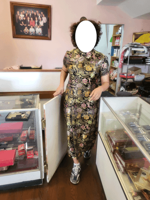 A person is wearing a black and coloured silk cheongsam. they're coming from behind the sewing counter.