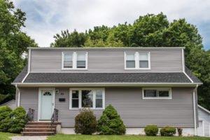 Granite gray vinyl siding, new windows with matching cladding, new shingled roof, and updated white 6″ gutters.