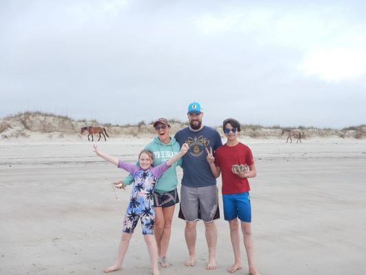 Our family posing on Cumberland Island Beach with wild horses passing in the background.