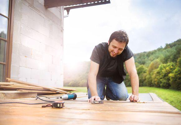 Smiling handyman installing wooden flooring in patio, working with hammer