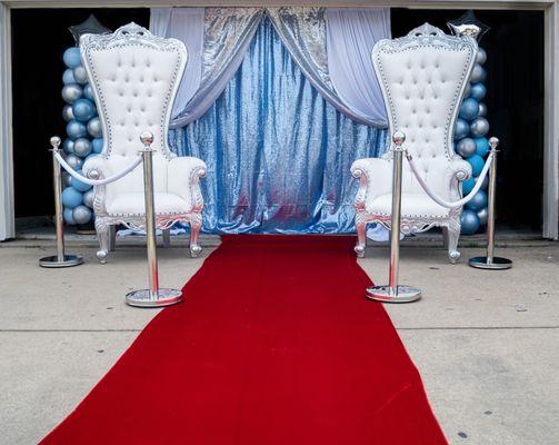 Red carpet runway with Silver trimmed throne chairs.  Silver and blue backdrop, along with matching balloon columns.