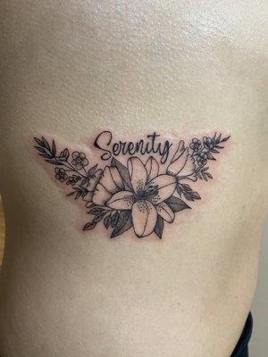 Tattoo of flowers with the word "serenity" on the ribs