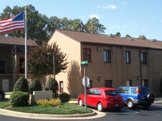 Building entrance is on the side right in back of the flag pole.