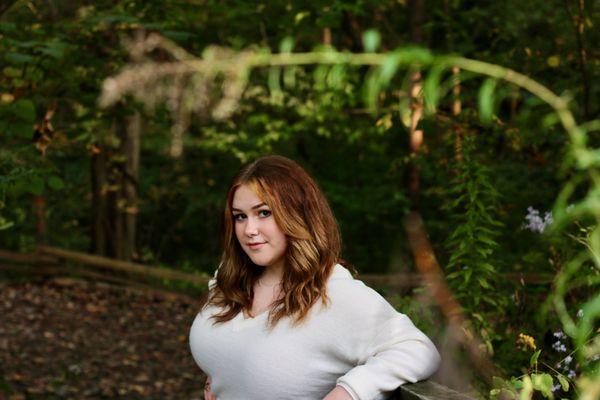 Emma leaning against a railing. There are trees in the background and foliage framing her. (Image chosen for Yelp's automatic  cropping.)