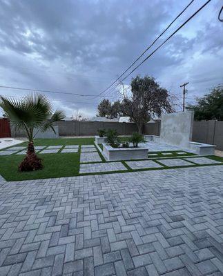 Grey paver with stepping pads, artificial turf, media wall, and planters